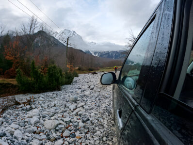 Woman sitting on an off-road car rentals in Albania's foggy northern wilderness, showcasing adventure travel with a spare tire on the roof rack.