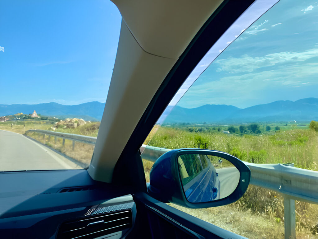 International Driving Permit for Albania: Do You Need One? 2 Scenic view from inside a car driving in Albania, featuring a clear blue sky, mountains, and a winding road with guardrails, highlighting the need for an International Driving Permit.