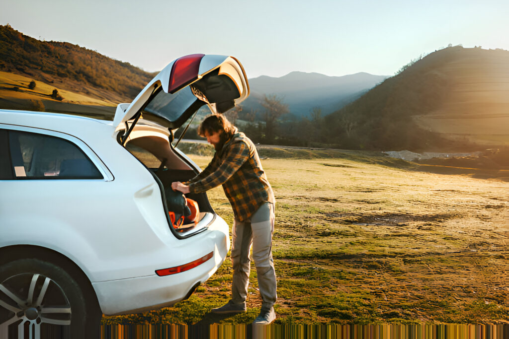 A person packing a car trunk with camping gear in a scenic mountainous landscape at sunset, ideal for planning a road trip and renting a car for the Albanian Riviera to discover its best routes and beaches.