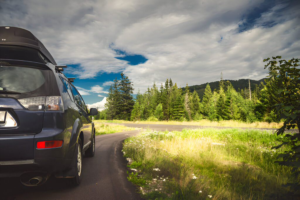 Dark SUV with a roof box driving on a scenic Albanian road surrounded by lush greenery and mountains, highlighting the freedom of exploring with a trusted car rental in Albania.