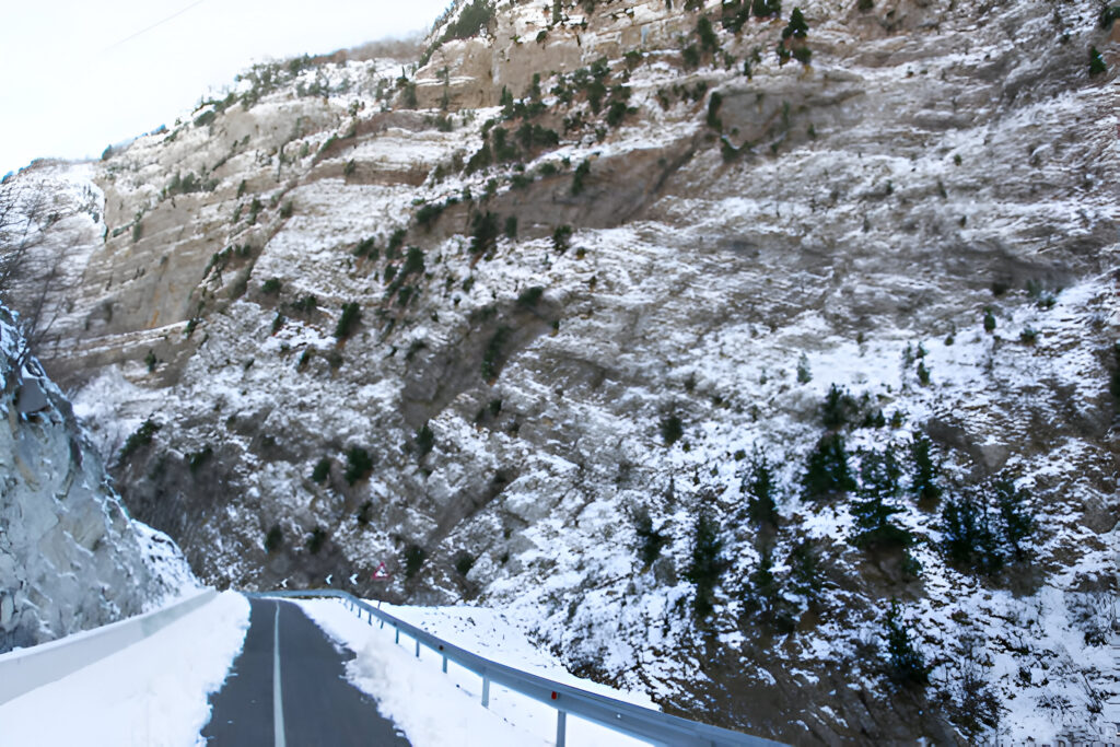 Winter in Albania: Best Mountain Drives 2 Snow-covered mountain road in Albania with a car in the distance, highlighting the stunning winter landscapes and scenic routes perfect for a winter in Albania road trip with essential car rental tips.